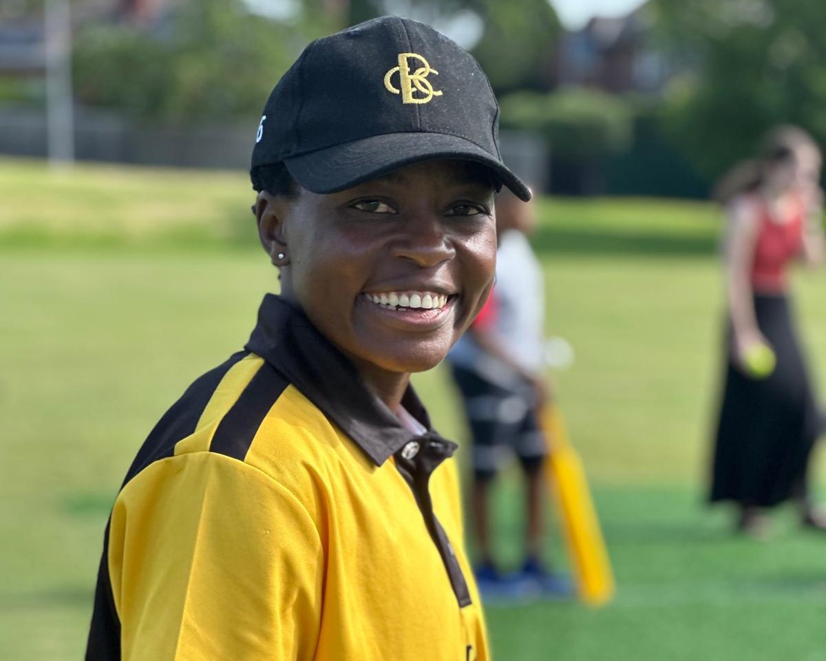 Close up profile image of a Zimbabwean cricketer wearing a yellow polo and black cap, smiling at the camera 