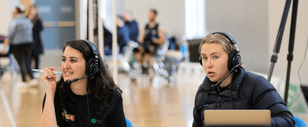 close up of two women wearing commentator headsets with microphones, speaking 