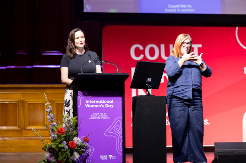 Sarah Styles stands at a lectern that says count her in, with an auslan interpreter next to her. 